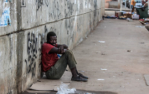 Homeless man in red shirt sitting on the sidewalk