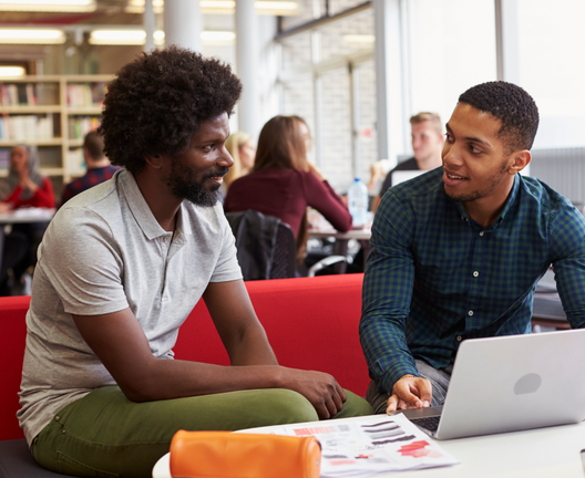 Two male students talking by a laptop computer