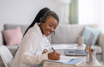 Young woman at computer with headset and writing