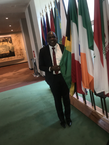 Senator Dr Floyd Morris stands beside flag of Jamaica at UN COSP